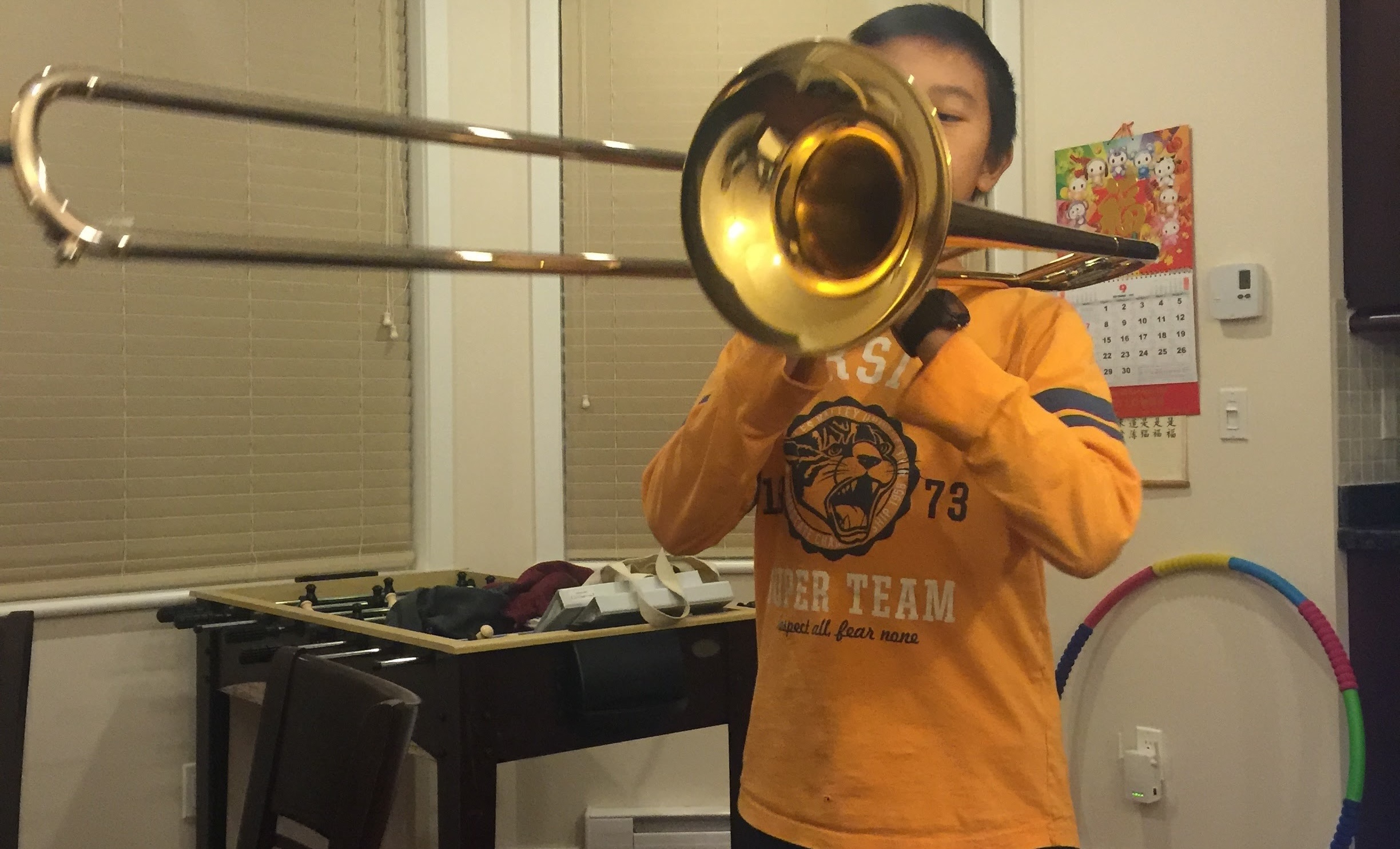 Kid blowing to a trombone at a living room environment