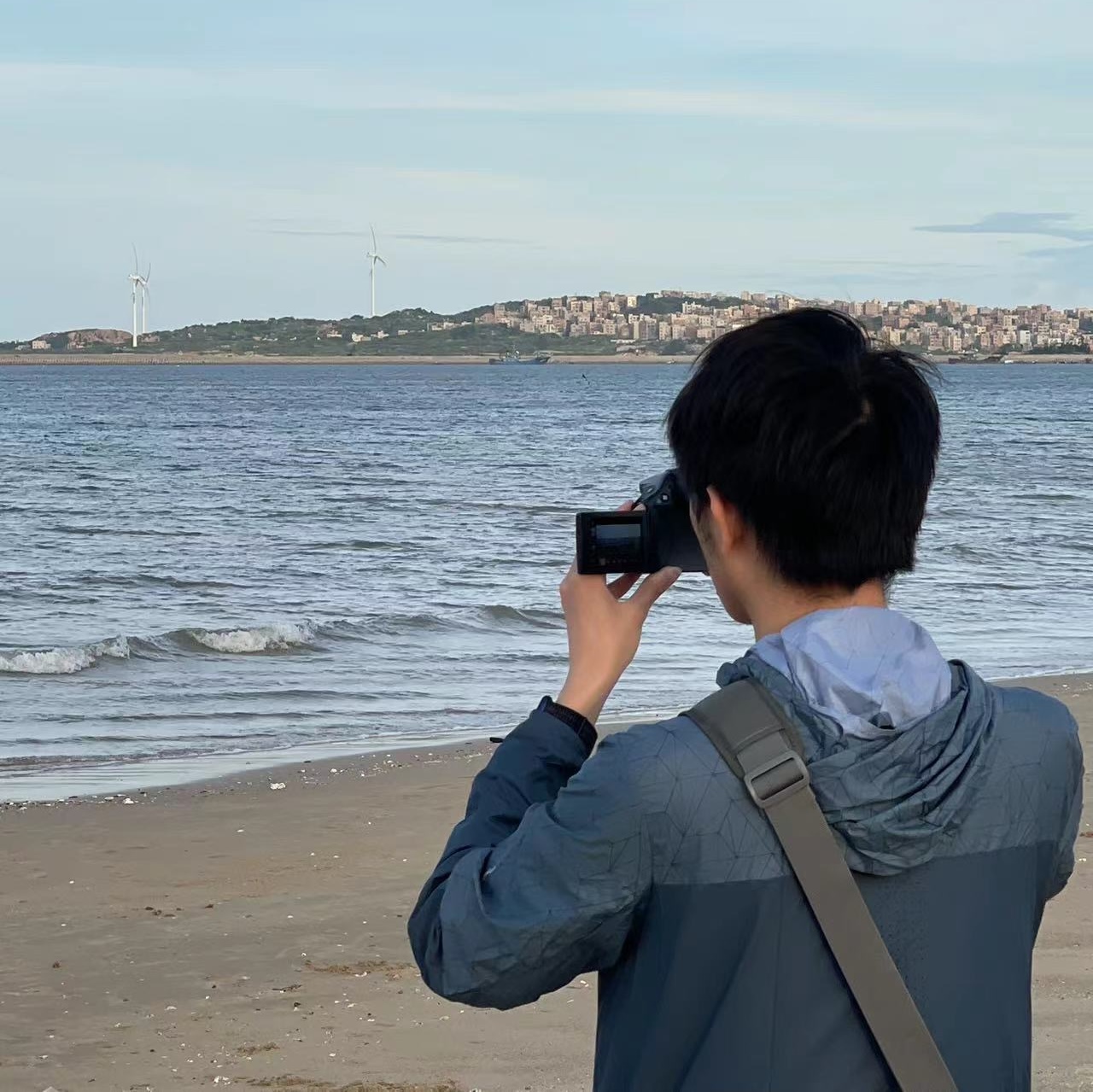 backside of body using a professional camera on a seashore with peninsula across the sea